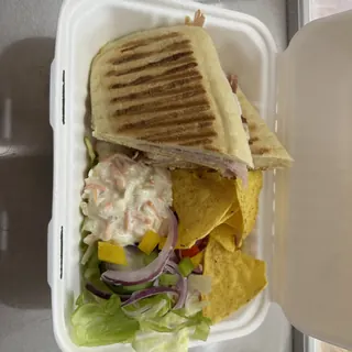 A takeaway panini box with side salad and crisps