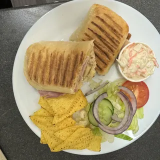 A toasted panini with side salad, coleslaw and crisps